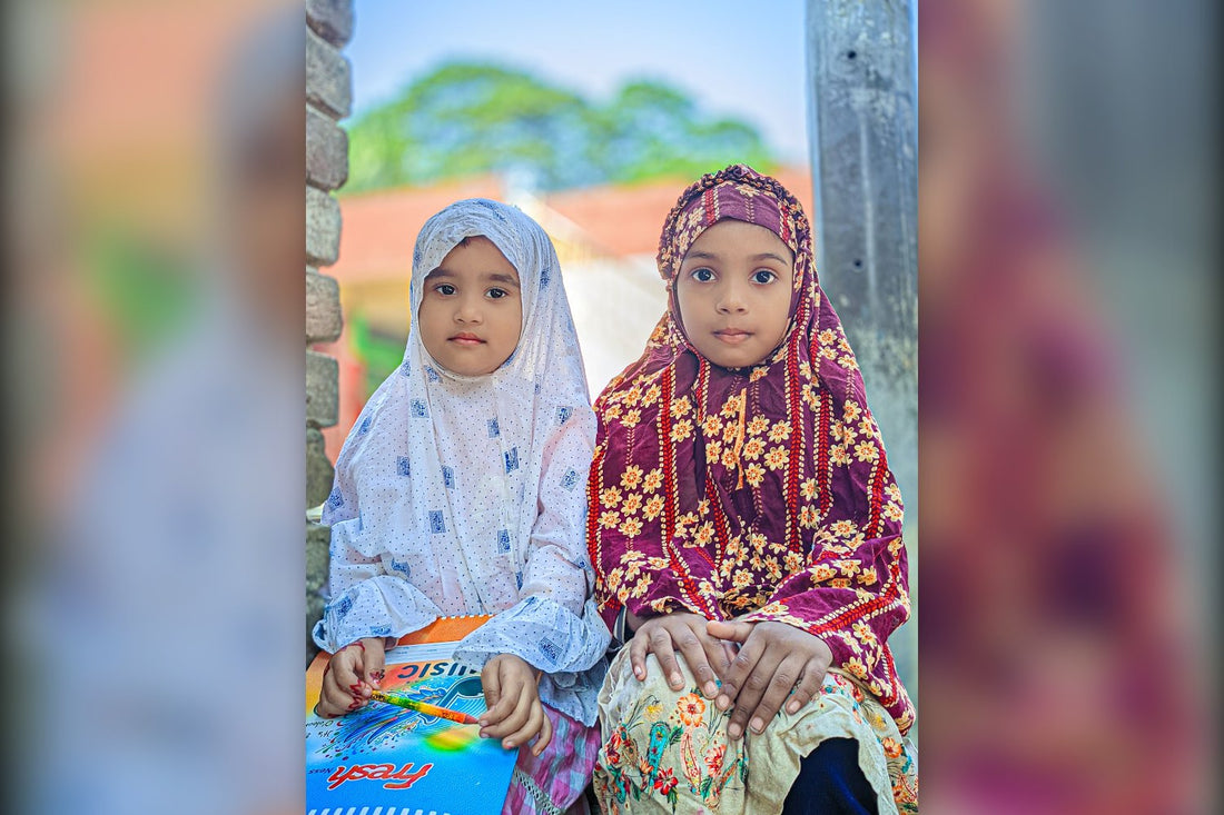 Two young Muslim girls in hijab sitting with a colouring book
