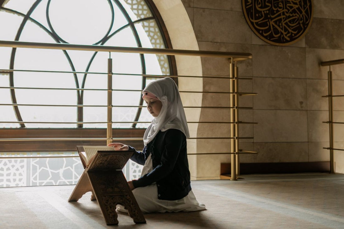 Muslim girl in a white hijab reading the Quran on a wooden rihal stand in a mosque